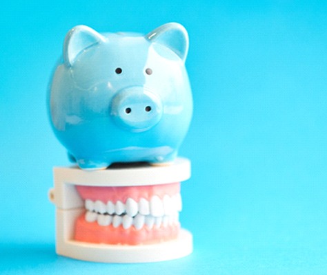 Piggy bank atop model teeth representing cost of Invisalign in Lancaster
