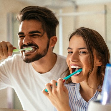 Couple smiling while brushing teeth in bathroom