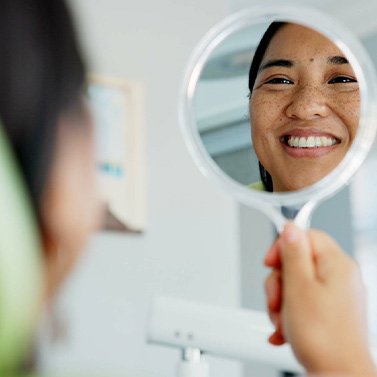 Woman smiling at reflection in handheld mirror