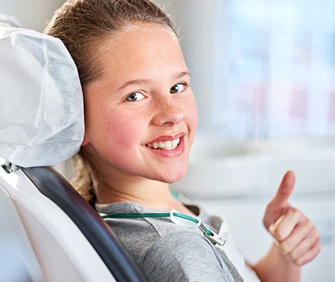 Little girl in dental chair giving thumbs up