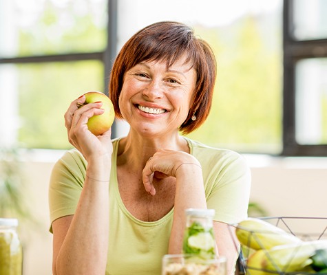 Woman smiling and eating an apple after denture stablization