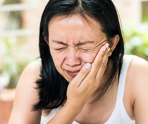 Woman holding cheek in pain before emergency dentistry