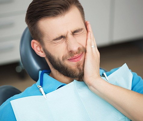 Man in need of emergency dentistry holding cheek in pain