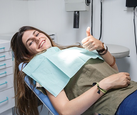 Woman in dental chair giving thumbs up after tooth extraction