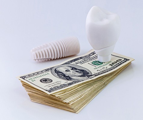 Model implant and money representing the cost of dental implants in Lancaster