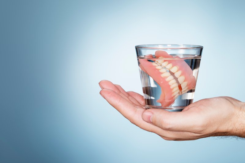 someone holding a pair of dentures in a glass