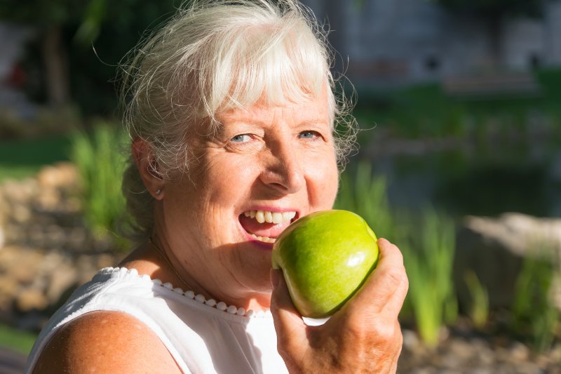 An older woman eating an apple with dentures