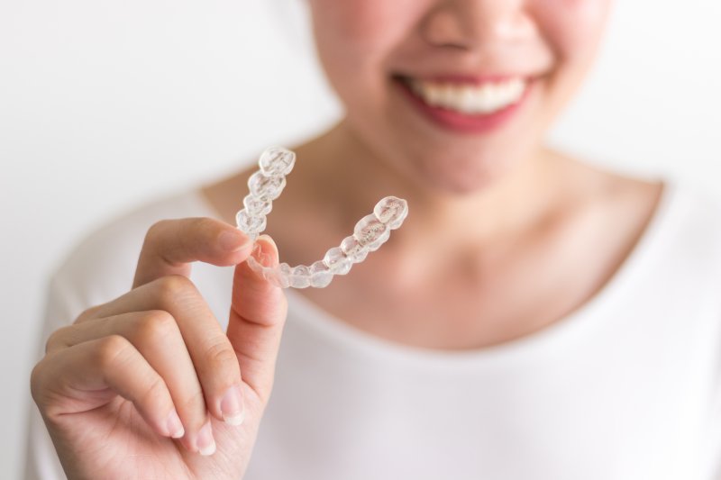 person holding an Invisalign aligner and smiling